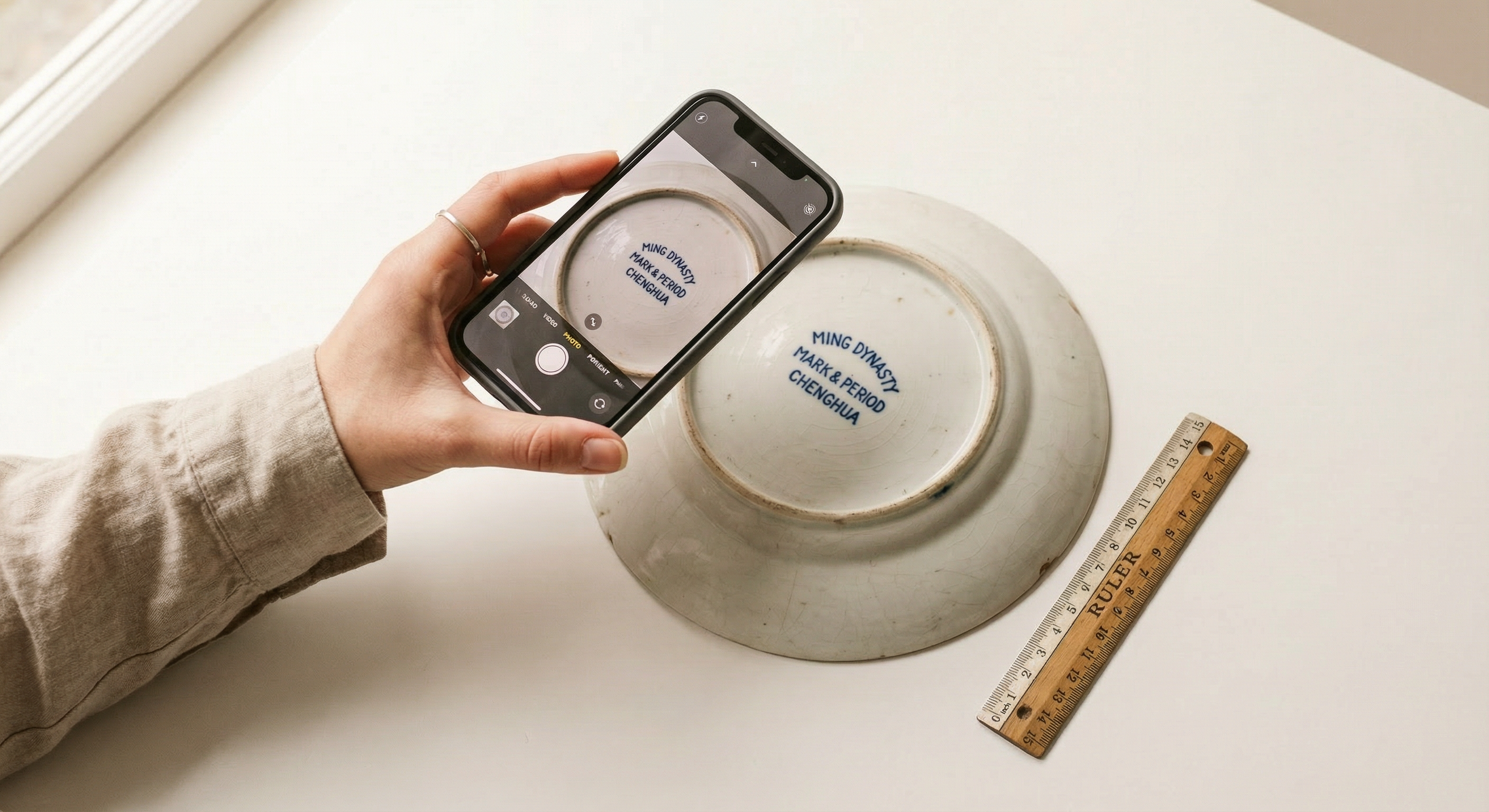 Smartphone fotografeert onderkant antiek porselein op witte achtergrond — authenticatie fotografie