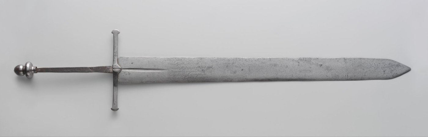 Long two-handed sword with a globular pommel, a straight crossguard and an engraved verse on the blade, lying on a grey background